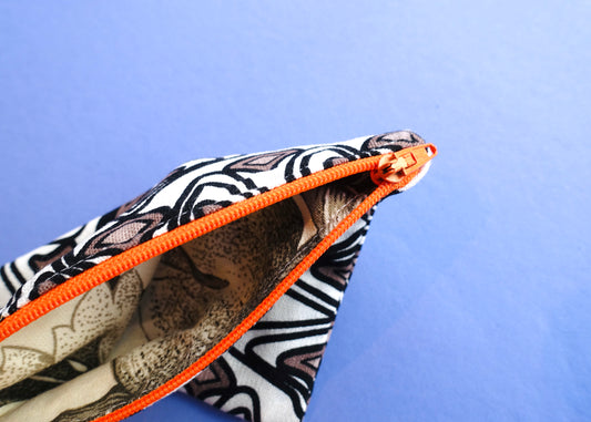 Etuitje in geometrische zwartwit print met oranje rits en beige bloemenvoering